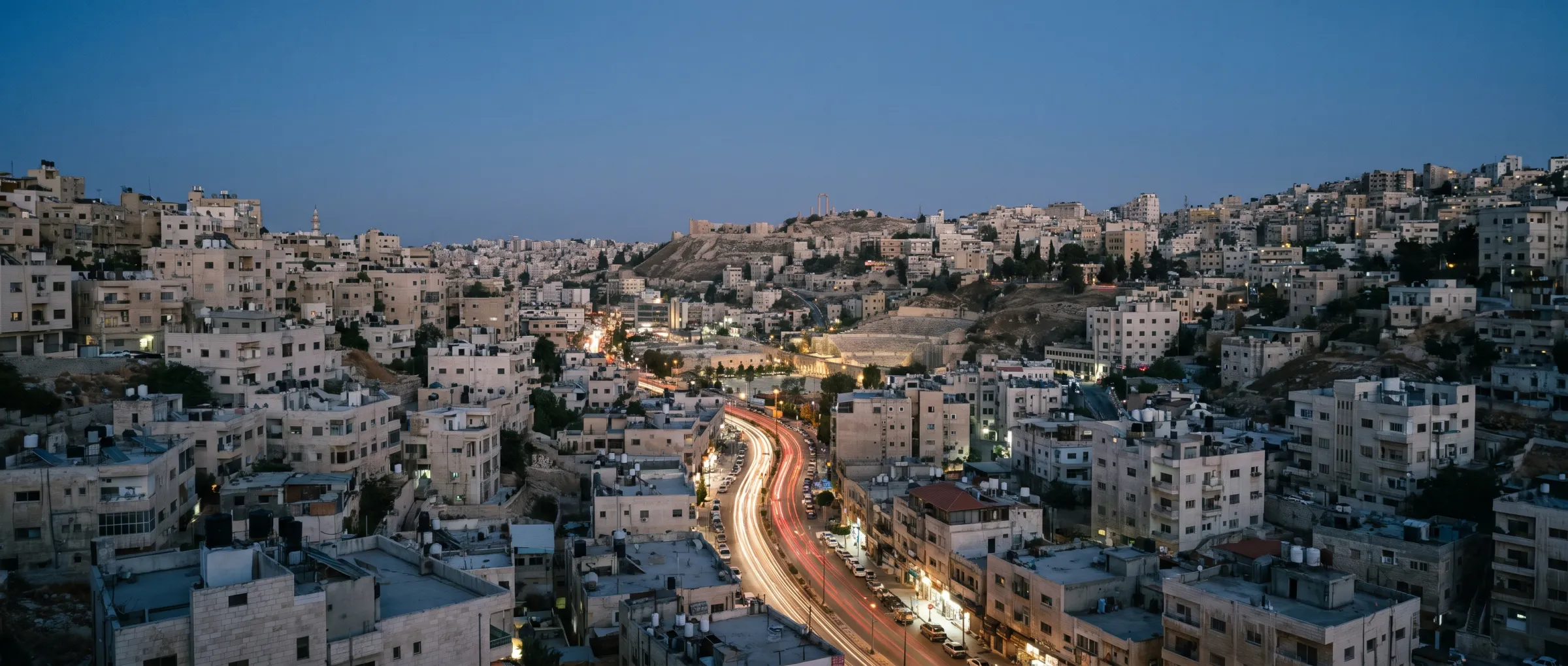 Amman at dusk, limestone hills stacked above the city road